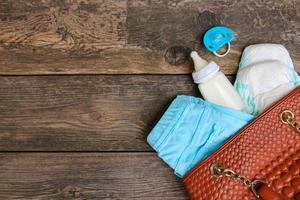 Women's handbag with items to care for the child on old wooden background photo