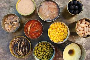 Different open canned food on old wooden background. Top view. Flat lay. photo