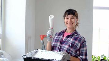 gelukkig vrouw in verf rol en wit verf voor muren in handen detailopname portret. bouw werk en kunstmatig reparaties in huis, muur schilderen, verven, afwerking werk met uw eigen handen video