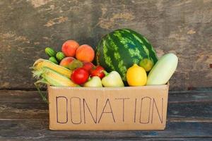 Donation box with vegetables and fruits on the old wooden background. photo