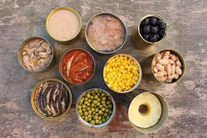 Different open canned food on old wooden background. Top view. Flat lay. photo