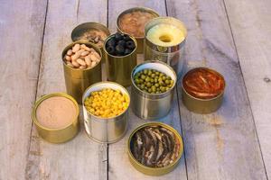 Different open canned food on old wooden background. photo