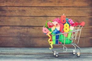 Shopping cart with items for birthday celebration on wooden background. Toned image.