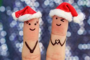 Fingers art of couple celebrates Christmas. Concept of man and woman laughing in new year hats. Boyfriend showing fingers in heart shape. Toned image. photo