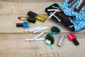 Cosmetics and cigarettes fell out of the backpack of a teenager on a wooden background. photo