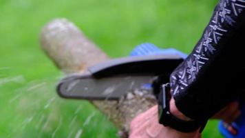 Hand-held portable camping electric saw on a battery for cutting firewood and wood. Close-up, a hand sawing a log, splinters flying video