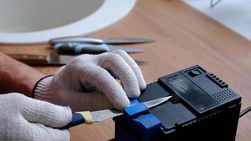 Schärfung ein Messer auf ein elektrisch Anspitzer beim heim. das des Mannes Hand fährt das Messer Klinge zwischen das Blau Spitzer, Staub fliegt auf das Maschine. 4k, schleppend Bewegung video