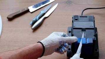 Sharpening a knife on an electric sharpener at home. The man's hand drives the knife blade between the blue sharpeners, dust flies on the machine. 4k, slow motion video