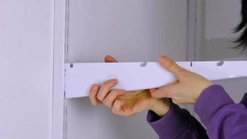 Installation brackets of a metal mesh shelf in the dressing room system on a bracket. Hands is assembling a white holder storage system close-up video