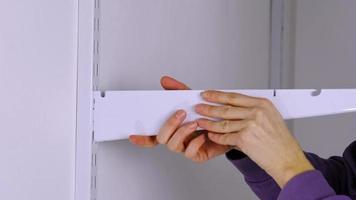 Installation brackets of a metal mesh shelf in the dressing room system on a bracket. Hands is assembling a white holder storage system close-up video