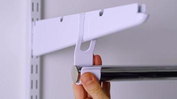 Installation brackets of a metal mesh shelf in the dressing room system on a bracket. Hands is assembling a white holder storage system close-up video