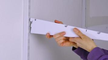 Installation brackets of a metal mesh shelf in the dressing room system on a bracket. Hands is assembling a white holder storage system close-up video