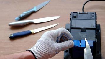 Sharpening a knife on an electric sharpener at home. The man's hand drives the knife blade between the blue sharpeners, dust flies on the machine. 4k, slow motion video