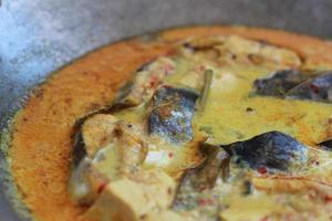 photo of tuna fish and white tofu in yellow spice sauce on a frying pan. Indonesian traditional food photo concept.