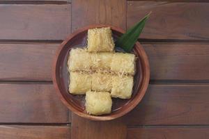 a close up of lupis with grated coconut and brown sugar sauce served in a wooden bowl. Indonesian traditional food photo concept.