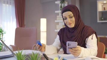 Woman in hijab shopping online. Muslim woman in hijab places orders online with a credit card. video