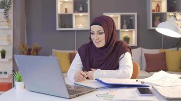 bedrijf vrouw in hijab werken van een afstand. moslim bedrijf vrouw in hijab maken een video telefoontje Aan een laptop, op zoek Bij grafieken.