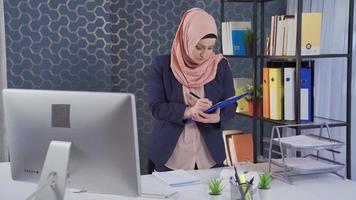 Muslim business woman in hijab takes and analyzes notes in office. A business woman in hijab is working, she needs to get her work done. video
