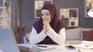 musulmán negocio mujer se regocija trabajando desde hogar. negocio mujer trabajando en hogar oficina es mirando a ordenador portátil y se regocija consiguiendo bueno noticias. video