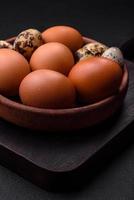 Raw chicken and quail eggs in a brown ceramic bowl on a dark concrete background photo