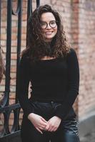 hermosa joven mujer con morena Rizado cabello, retrato en ojo lentes disfrutando el Dom en el ciudad. foto