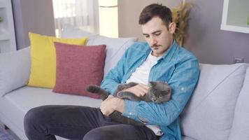 Thoughtful man loves his gray cat. Thoughtful man loves his cat in his arms at home.