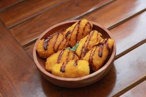 a close up of banana nuggets with chocolate sauce topping served on a wooden bowl. Food concept photo. photo