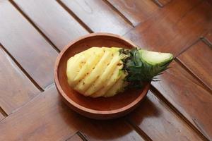 a close up of a peeled pineapple on a wooden bowl. fruit photo concept.