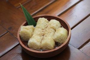 a close up of lupis with grated coconut and brown sugar sauce served in a wooden bowl. Indonesian traditional food photo concept.