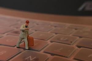 un miniatura figura de un oficina trabajador que lleva un maletín caminando Entre el teclados. foto