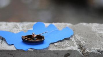 a miniature figure of a fisherman fishing in a river visualized on blue paper cutouts. photo