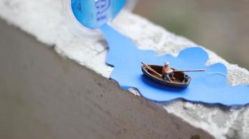 a miniature figure of a fisherman fishing in a river visualized on blue paper cutouts. photo