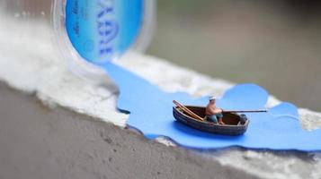 un miniatura figura de un pescador pescar en un río visualizado en azul papel recortes foto