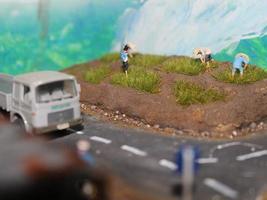 a miniature diorama of a rice field and a road as well as several people and vehicles and buildings. photo