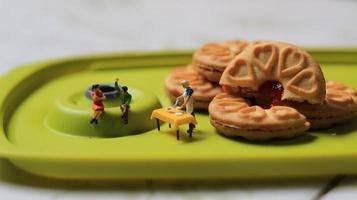 miniatura cifras de un Pareja hablando en un verde comida mesa cerca un cocinero Cocinando en un antecedentes de un pastel lleno con fresa mermelada. discusión concepto. foto