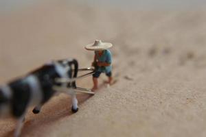 miniatura figura de un granjero arada un campo con su vaca en un cartulina. foto