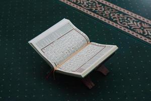 un cerca arriba de el santo libro Al Quran en un verde oración alfombra. islámico foto concepto.