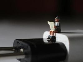 un cerca arriba de un miniatura figura de un persona leyendo encima un célula teléfono cargador. foto