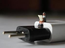 a close up of a miniature figure of a person reading above a cell phone charger. photo