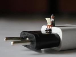 a close up of a miniature figure of a person reading above a cell phone charger. photo