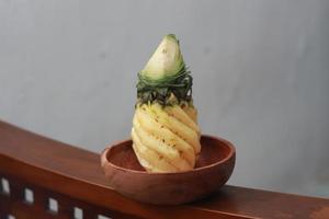 a close up of a peeled pineapple on a wooden bowl. fruit photo concept.
