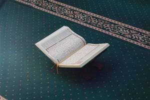 un cerca arriba de el santo libro Al Quran en un verde oración alfombra. islámico foto concepto.