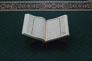 un cerca arriba de el santo libro Al Quran en un verde oración alfombra. islámico foto concepto.