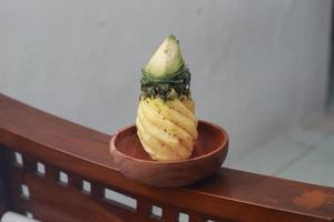 a close up of a peeled pineapple on a wooden bowl. fruit photo concept.