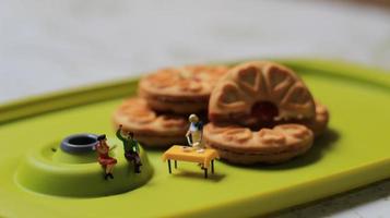 miniatura cifras de un Pareja hablando en un verde comida mesa cerca un cocinero Cocinando en un antecedentes de un pastel lleno con fresa mermelada. discusión concepto. foto