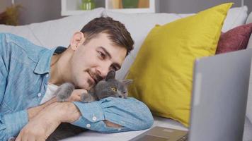 giovane uomo guardare a il computer con il suo grigio gatto. giovane uomo con gatto proprietario guardare a il computer portatile e Guardando qualche cosa. video