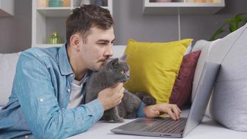 hombre y gato mirando a ordenador portátil juntos. el gato mira a el ordenador portátil en sorpresa. video
