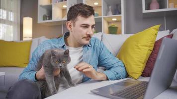 el hombre trabajos a el ordenador portátil y ama su gato. el hombre quien trabajos a hogar en el ordenador portátil ama su gato en su regazo. video