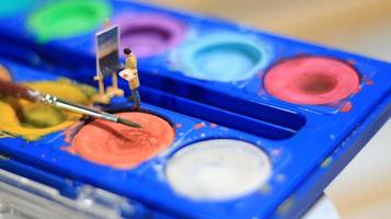 a miniature figure of a painter painting a landscape on watercolors. artist concept. photo