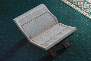 un cerca arriba de el santo libro Al Quran en un verde oración alfombra. islámico foto concepto.